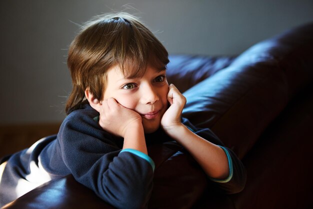 Young boy with his hands propping up his head sitting on couch