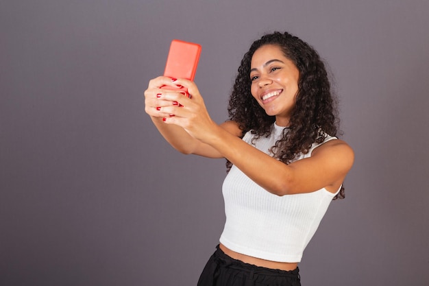 Young Brazilian black woman taking selfie self portrait with red cellphone