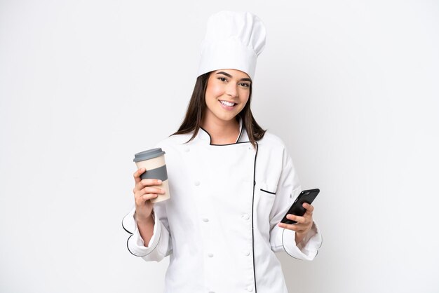 Young Brazilian chef woman isolated on white background holding coffee to take away and a mobile