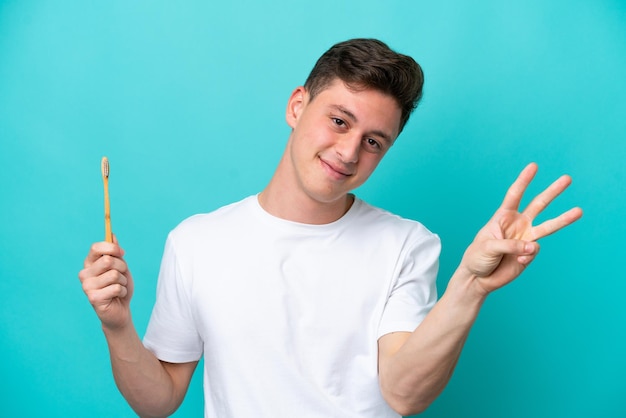 Young Brazilian man brushing teeth isolated on blue background happy and counting three with fingers