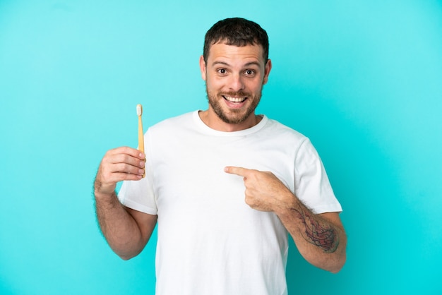 Young Brazilian man brushing teeth isolated on blue background with surprise facial expression