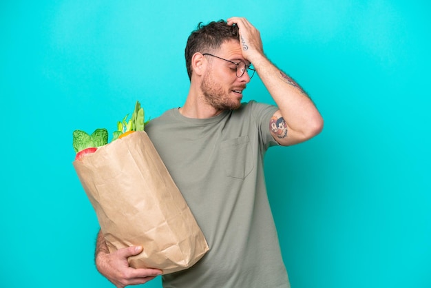 Young Brazilian man holding a grocery shopping bag isolated on blue background has realized something and intending the solution