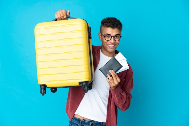 Young Brazilian man over isolated background in vacation with suitcase and passport