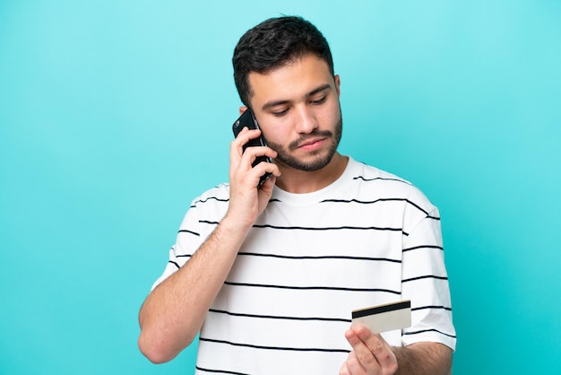 Young Brazilian man isolated on blue background buying with the mobile with a credit card