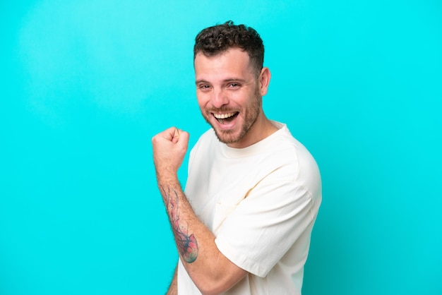 Young Brazilian man isolated on blue background celebrating a victory