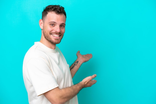 Young Brazilian man isolated on blue background extending hands to the side for inviting to come