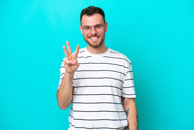 Young Brazilian man isolated on blue background happy and counting three with fingers