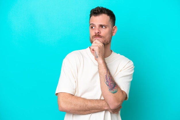 Young Brazilian man isolated on blue background having doubts and thinking