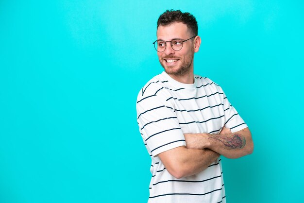 Young Brazilian man isolated on blue background looking to the side and smiling