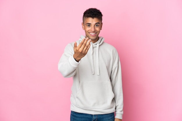 Young Brazilian man isolated on pink wall inviting to come with hand. Happy that you came