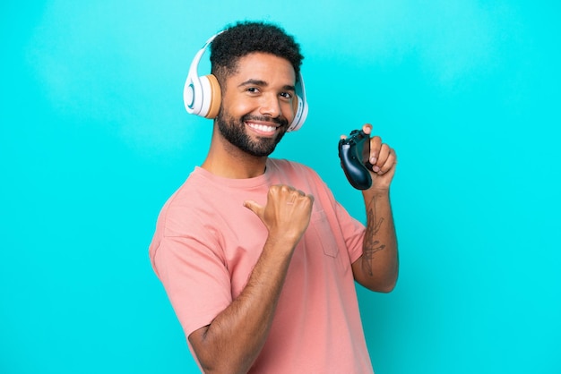 Young brazilian man playing with a video game controller isolated on blue background proud and selfsatisfied