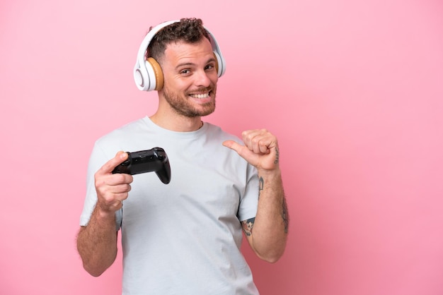 Young Brazilian man playing with video game controller isolated on pink background proud and selfsatisfied