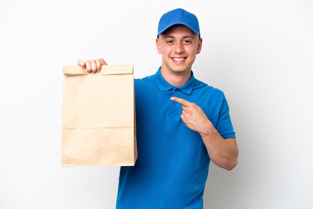 Young Brazilian man taking a bag of takeaway food isolated on white background pointing to the side to present a product