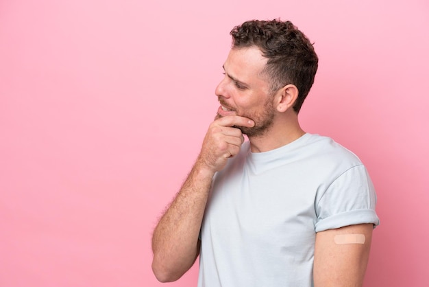 Young Brazilian man wearing a bandaids isolated on pink background thinking an idea and looking side