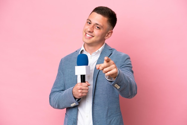 Young brazilian presenter man isolated on pink background pointing front with happy expression