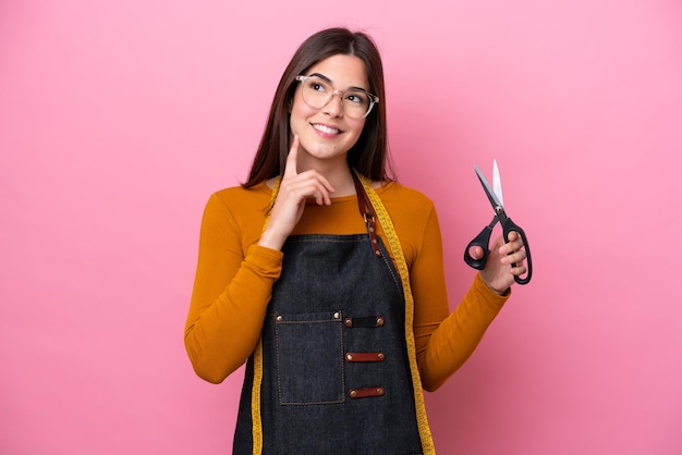 Young Brazilian seamstress woman isolated on pink background thinking an idea while looking up