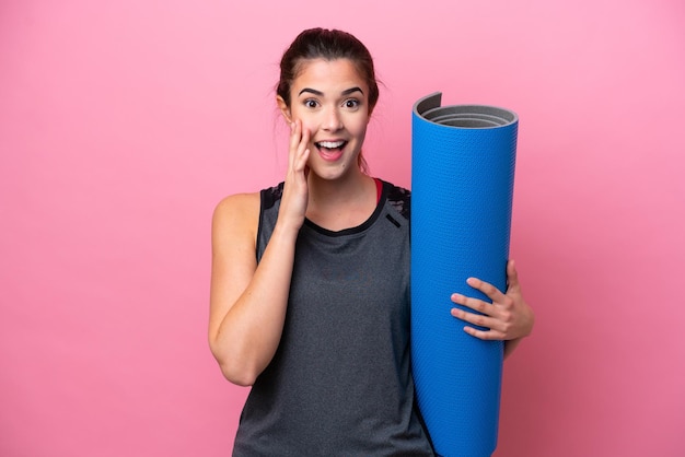 Young Brazilian sport woman going to yoga classes while holding a mat isolated on pink background with surprise and shocked facial expression