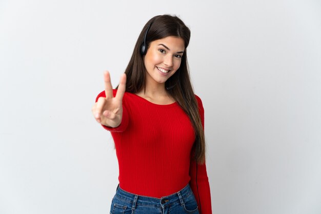 Young Brazilian telemarketer girl over isolated wall smiling and showing victory sign