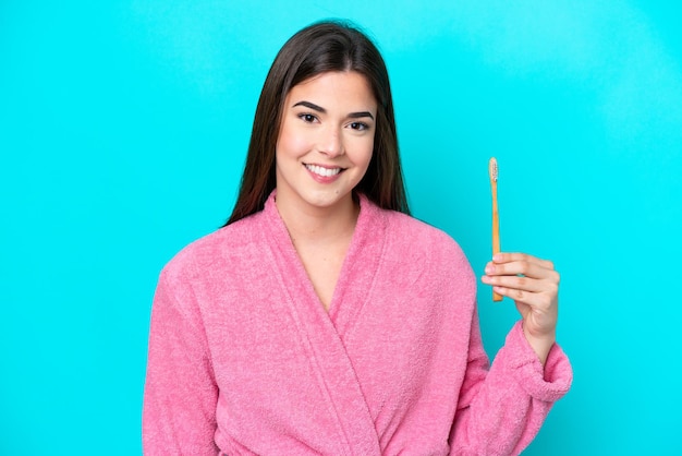 Young Brazilian woman brushing teeth isolated on blue background smiling a lot