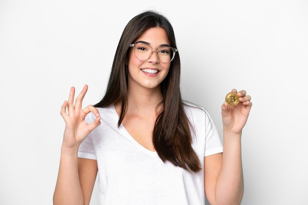 Young Brazilian woman holding a Bitcoin isolated on white background showing ok sign with fingers