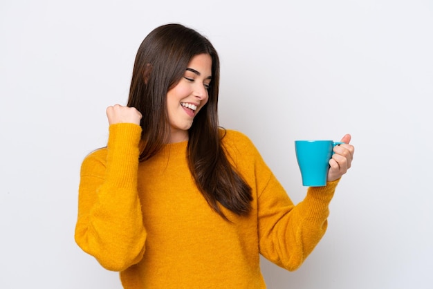 Young Brazilian woman holding cup of coffee isolated on white background celebrating a victory