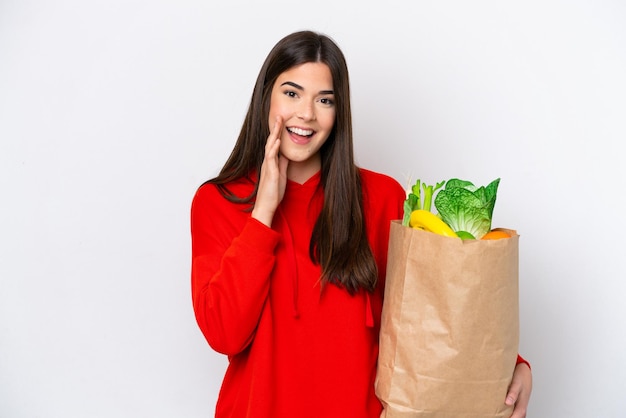 Young Brazilian woman holding a grocery shopping bag isolated on white background shouting with mouth wide open