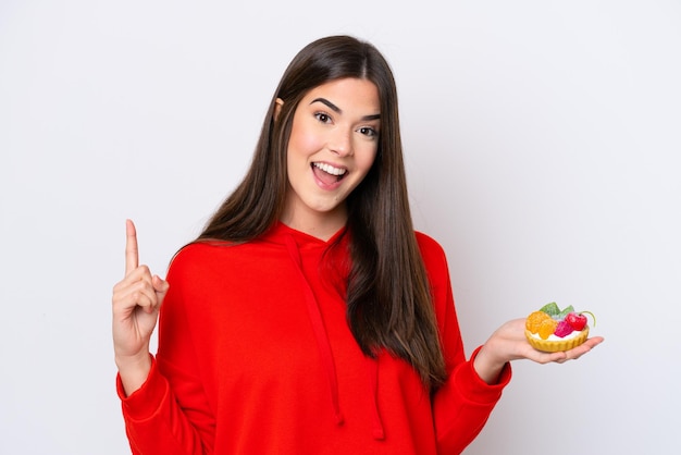 Young Brazilian woman holding a tartlet isolated on white background pointing up a great idea