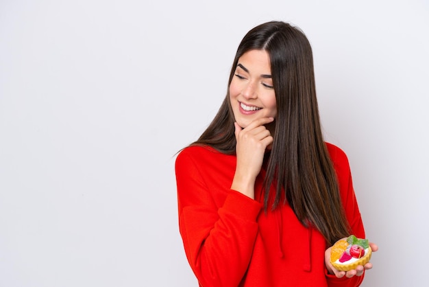 Young Brazilian woman holding a tartlet isolated on white background thinking an idea and looking side