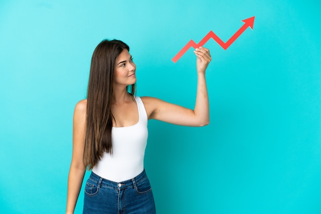 Young Brazilian woman isolated on blue background holding a catching a rising arrow with happy expression