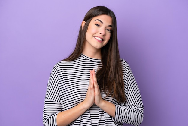 Young Brazilian woman isolated on purple background keeps palm together Person asks for something