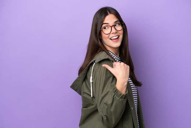 Young Brazilian woman isolated on purple background pointing to the side to present a product