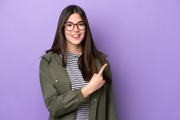 Young Brazilian woman isolated on purple background pointing to the side to present a product