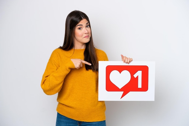 Young Brazilian woman isolated on white background holding a placard with Like icon and pointing it