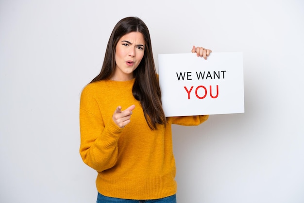 Young Brazilian woman isolated on white background holding We Want You board and pointing to the front