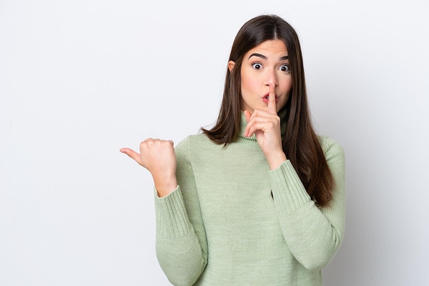 Young Brazilian woman isolated on white background pointing to the side and doing silence gesture