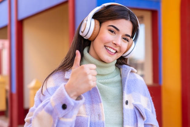 Young Brazilian woman at outdoors listening music and with thumb up