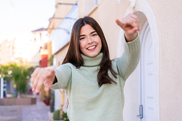 Young Brazilian woman at outdoors points finger at you while smiling