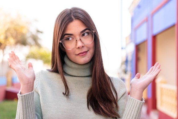 Young Brazilian woman at outdoors With glasses and having doubts