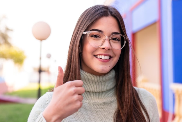 Young Brazilian woman at outdoors With glasses and with thumb up