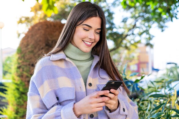 Young Brazilian woman in a park sending a message with the mobile