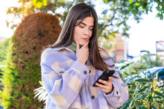 Young Brazilian woman in a park thinking and sending a message