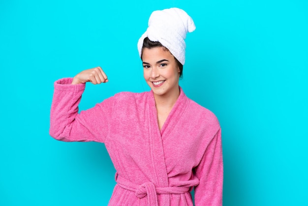 Young Brazilian woman with a bathrobe isolated on blue background doing strong gesture