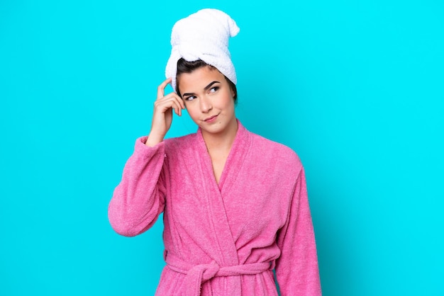 Young Brazilian woman with a bathrobe isolated on blue background having doubts and with confuse face expression