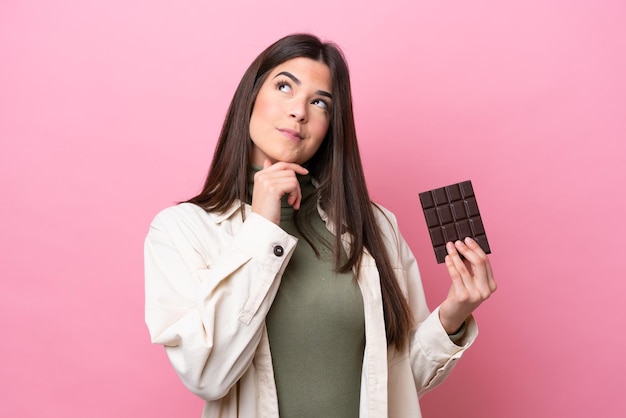 Young Brazilian woman with chocolat isolated on pink background and looking up