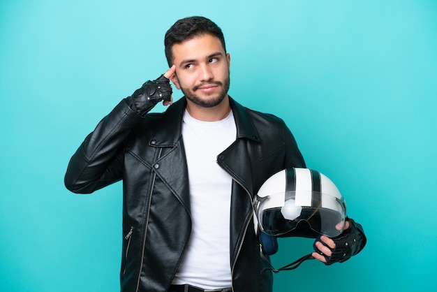 Young Brazilian woman with a motorcycle helmet isolated on blue background having doubts and thinking