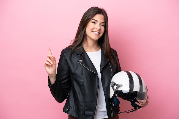 Young Brazilian woman with a motorcycle helmet isolated on pink background showing and lifting a finger in sign of the best