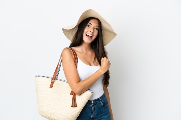 Young Brazilian woman with Pamela holding a beach bag isolated on white background celebrating a victory