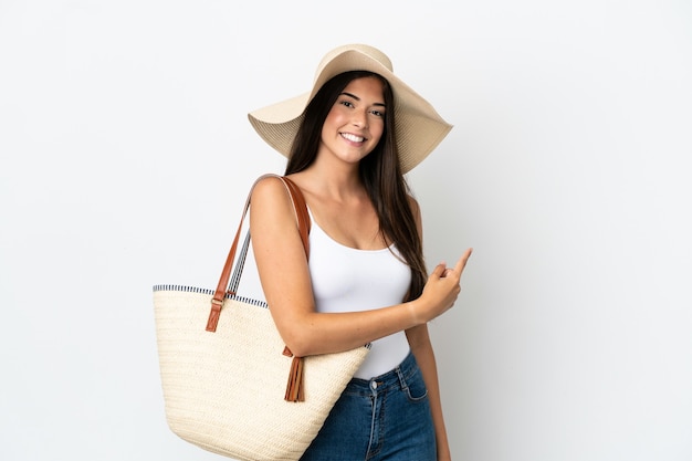 Young Brazilian woman with Pamela holding a beach bag isolated on white background pointing back