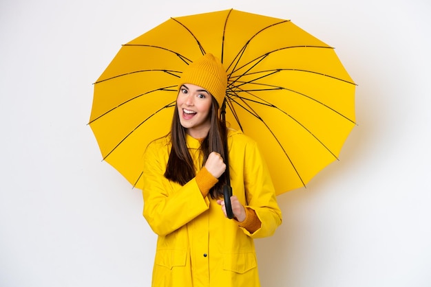 Young Brazilian woman with rainproof coat and umbrella isolated on white background celebrating a victory