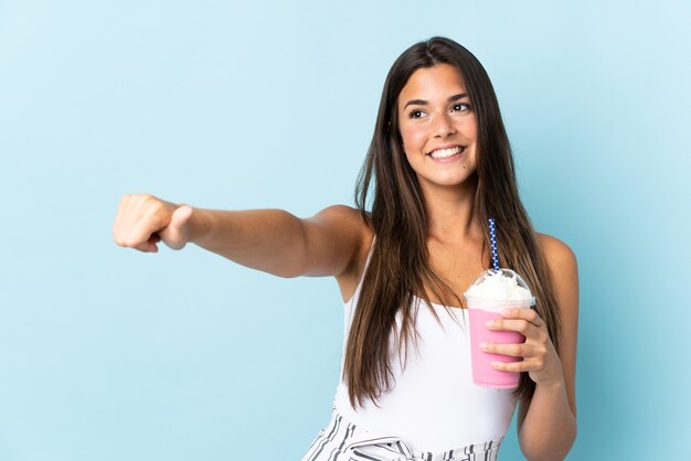 Young brazilian woman with strawberry milkshake isolated on blue background giving a thumbs up gesture